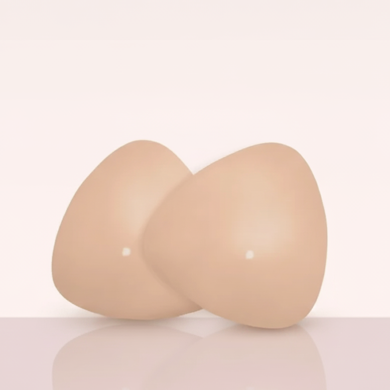 Paar Ultra Boostelle Silikon-Brusteinsätze in hautfarben/nude, auf glänzender Oberfläche mit weichem, femininen Hintergrund. Unsichtbare Einlagen für Volumen und perfekte Passform.
